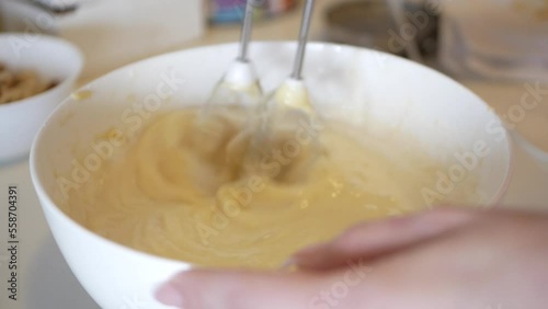 Female hands beat ingredients for dough with hand mixer on wooden kitchen table. Blender mixes the ingredients for pancakes.