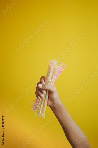 child hand holding many straw straws against yellow background 