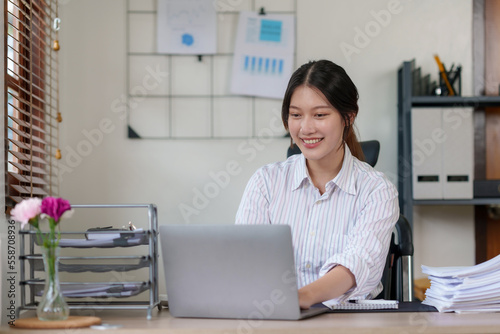 Attractive Asian businesswoman using laptop in office working attentively and happily.