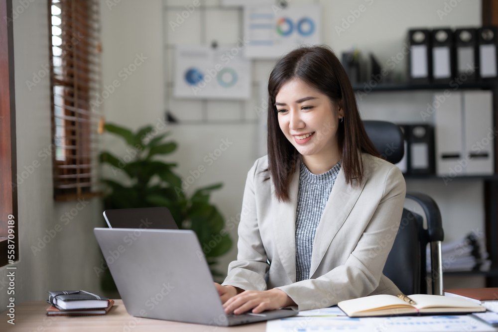 Attractive Asian businesswoman using laptop in office working attentively and happily. Attractive Asian businesswoman using laptop in office working attentively and happily.