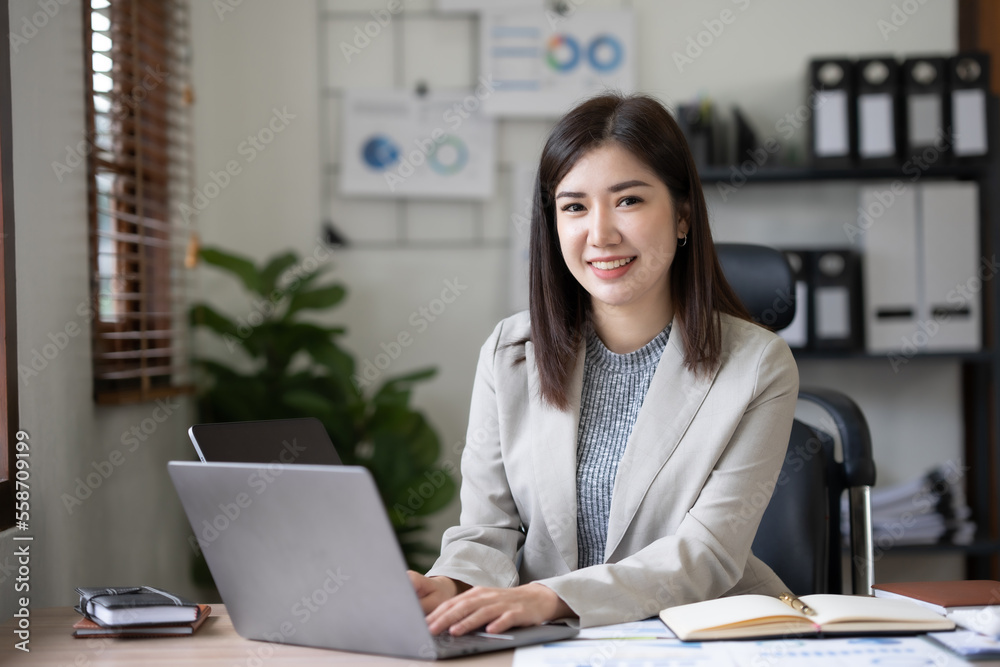 Attractive Asian businesswoman using laptop in office working attentively and happily. Attractive Asian businesswoman using laptop in office working attentively and happily.