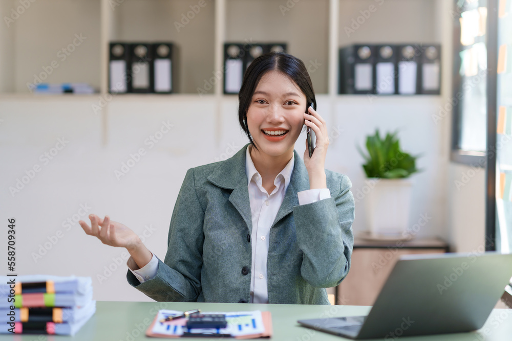 Smiling Asian businesswoman enjoying the phone, answering questions, talking to customers on the phone and comment in the office.