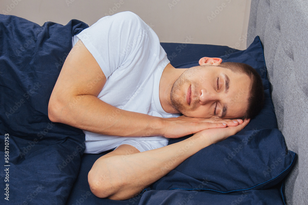 Top view of a handsome young man sleeping comfortably on the bed at night in his bedroom. Sleep in different positions. Bachelor bedroom. Deep sleep. Top view of a handsome young man sleeping comfortably on the bed at night in his bedroom. Sleep in different positions. Bachelor bedroom. Deep sleep.
