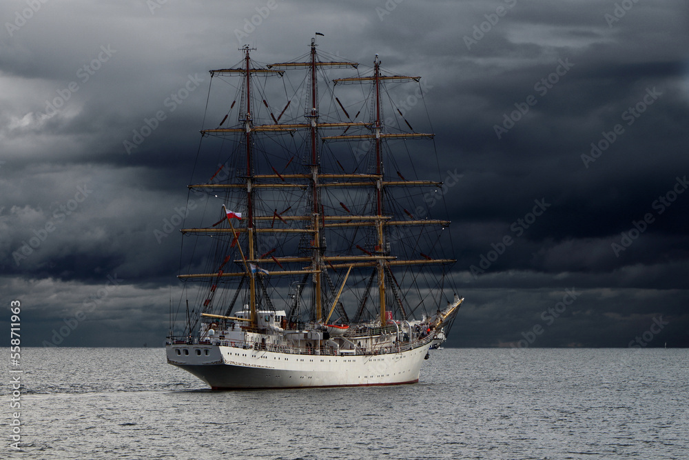 Three-masted sailing frigate goes to sea from the port against a stormy sky. Three-masted sailing frigate goes to sea from the port against a stormy sky.