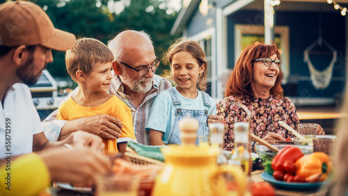 Photography Portrait of a Happy Senior Grandfather Holding His Bright Talented Little Grandchildren on Lap at a Outdoors Dinner Party with Food and Drinks