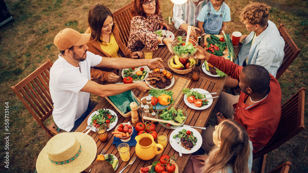 © Gorodenkoff - Top Down Elevated View at a Family and Friends Celebrating Outside at Home. Diverse Group of Children, Adults and Seniors Sitting at a Table, Having Fun Conversations. Eating Barbecue and Vegetables.