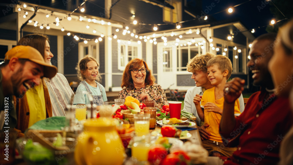 Grandmother Telling Funny Childhood Stories to Her Diverse Family and Multicultural Friends During a Festive Outdoors Dinner Table with Grilled Barbecue Meat and Lots of Fresh Vegetables.