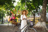 Portrait of Asian peddler with bike and flowers, Vietnamese woman girl traveling in Hanoi urban city town, Vietnam. People lifestyle.