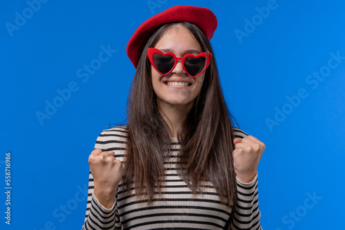 Pretty stylish woman with triumph yes gesture of victory  she achieved result  goals. Woman glad  happy  surprised excited happy lady on blue background. Jackpot concept.