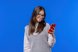 Pretty teenager surfing internet on smartphone. Girl with smile and joy on blue background. Tech, success, happiness, social networks concept.