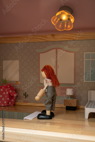 Wooden doll indoors with light in a dollhouse.