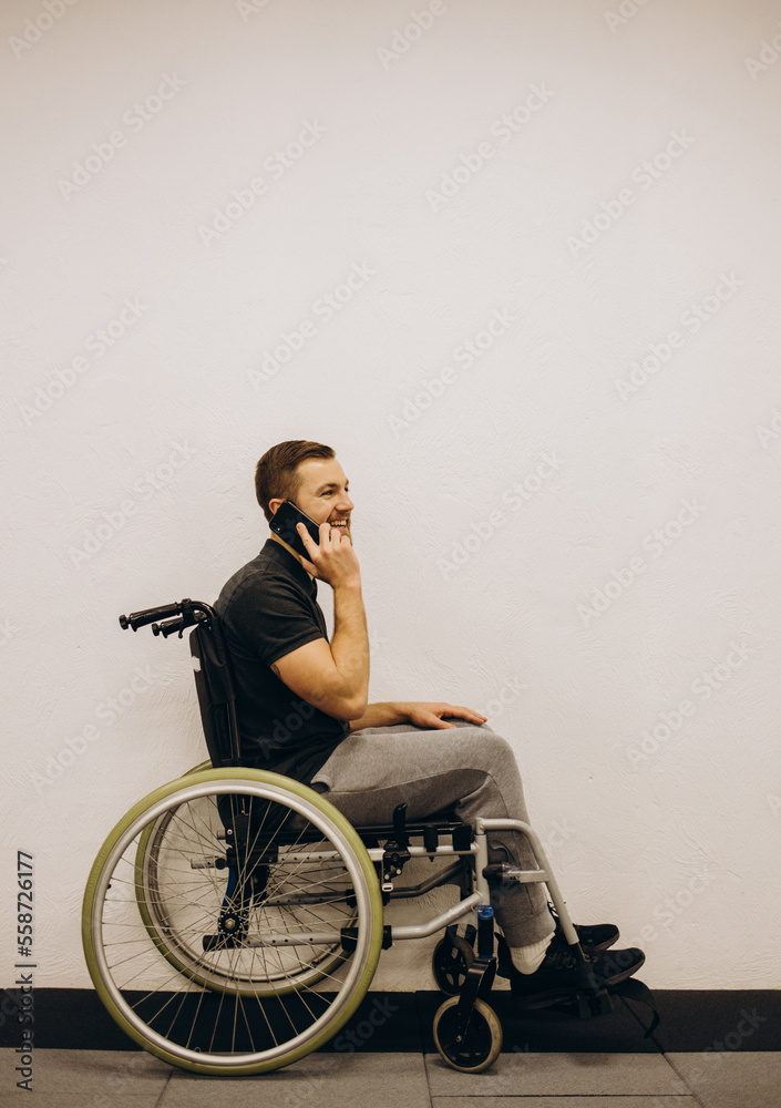 The disabled person sits in a wheelchair. He is talking to someone on his smartphone. He is in his large bright living room. He smiles. The disabled person sits in a wheelchair. He is talking to someone on his smartphone. He is in his large bright living room. He smiles.