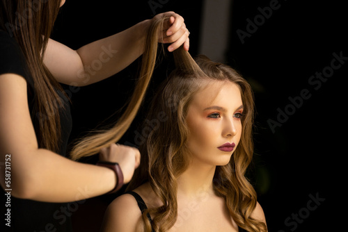 Professional hair stylist prepares woman makes curls hairstyle in a beauty salon. Long light brown natural hair.