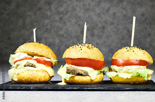 three homemade burger with cheese and meat, tomato and salad in blackboard plate