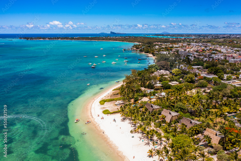 Fototapeta premium Mauritius - aerial landscape view along the coastline at Troy aux Biches Beach and Mont Choisy Beach in the background, with people walking on beach and boats swimming in the water of Indian Ocean 