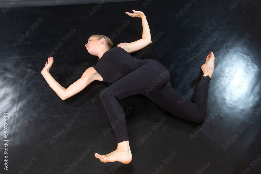 Young woman in a black onesie, doing a lying spinal twist.