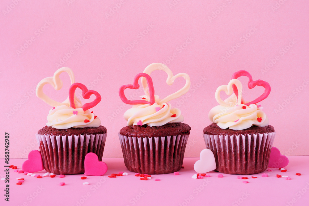 Valentines Day theme red velvet cupcakes with sweet hearts and creamy icing. Side view with a pink background. Valentines Day theme red velvet cupcakes with sweet hearts and creamy icing. Side view with a pink background.