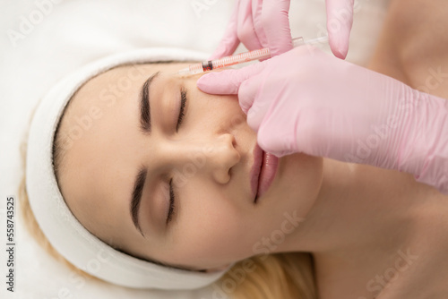 Close-up of the hands of an expert cosmetologist injecting botox into a woman s forehead. Correction of forehead and eye wrinkles with botulinum toxin.