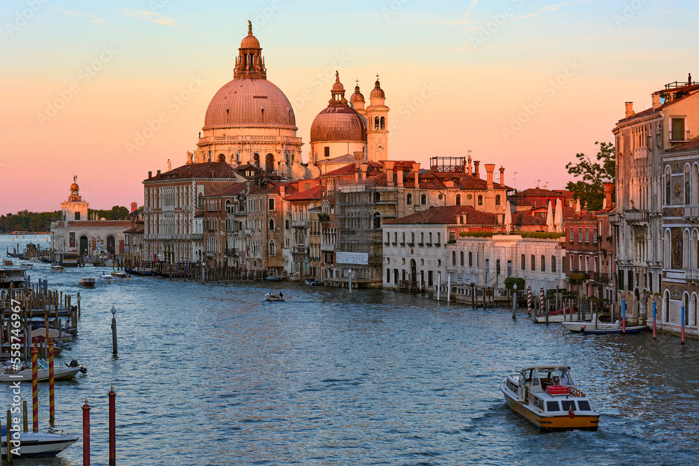 View of Santa Maria della Salute Cathedral surrounded by boats on the Grand Canal at sunset in Venice, Italy.