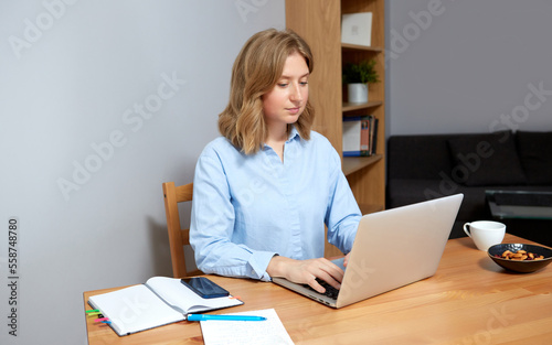 Young happy woman sitting at desk, working on computer at home.