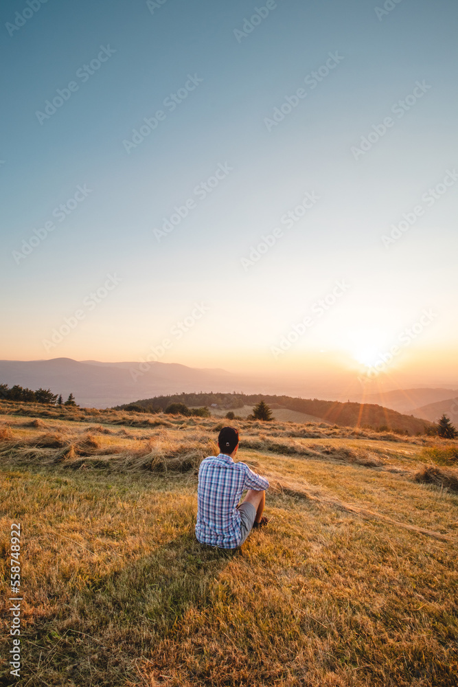 Man in shirt resting on grass watching sunset on a mountain in Beskydy mountains, Czech republic. Soaking up positive energy and relieving stress