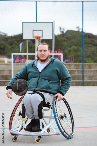 disabled man in wheelchair looking at camera and holding ball in open basketball court