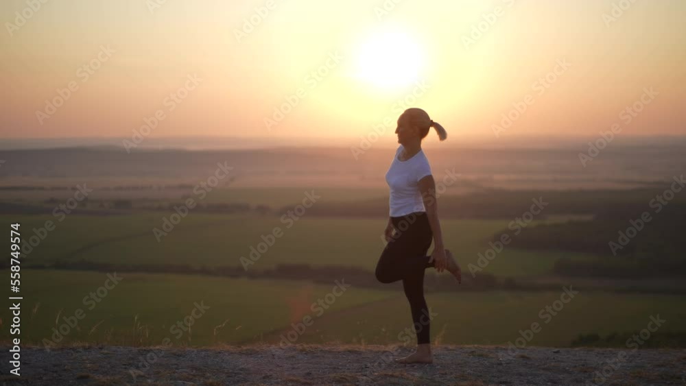 Silhouette of unrecognizable flexible yogi woman practicing yoga balancing on one leg stretching outdoor standing on top of mountains with beautiful landscape, on background of sunlight during sunset. Silhouette of unrecognizable flexible yogi woman practicing yoga balancing on one leg stretching outdoor standing on top of mountains with beautiful landscape, on background of sunlight during sunset.