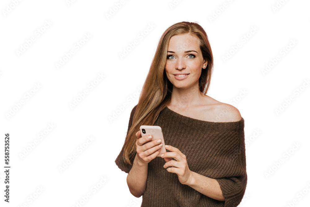 Beautiful young redhead woman dressed in brown knitted sweater with open shoulder, holds her smartphone, smiling, satisfied by talk with boyfriend, posing over transparent background with copy space Beautiful young redhead woman dressed in brown knitted sweater with open shoulder, holds her smartphone, smiling, satisfied by talk with boyfriend, posing over transparent background with copy space