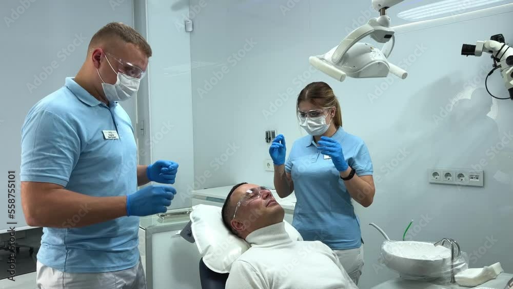 expensive dental clinic professional equipment doctor and nurse put on glasses they stand next to the patient all dressed light clothes blue and white in the frame are ready to do teeth cleaning expensive dental clinic professional equipment doctor and nurse put on glasses they stand next to the patient all dressed light clothes blue and white in the frame are ready to do teeth cleaning