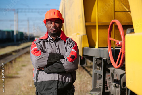 African american railway worker stands at freight train terminal
