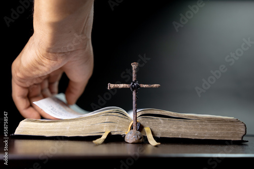 Leyendo la biblia, mano pasando de página, bendiciendo santa biblia y cruz de clavos en escritorio.