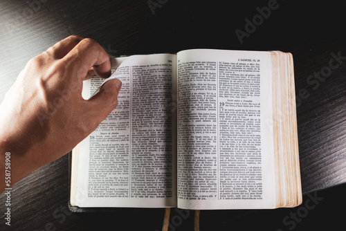Leyendo la biblia, mano pasando de página, bendiciendo santa biblia y cruz de clavos en escritorio.