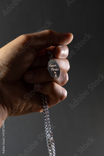 Mano sosteniendo collar con placa que tiene grabada la frase “nunca pierdas la fe” en fondo negro y blanco y negro. photo