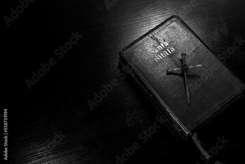 Portada de santa biblia en una meza y clavos oxidados formando una cruz encima del escritorio de pintura negra y destellos de luz. photo