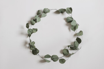 Green floral frame made of dry eucalyptus tree leaves and branches. Decorative wreath isolated on white table background. Minimal natural composition. Flat lay, top view. No people. Elegant web banner