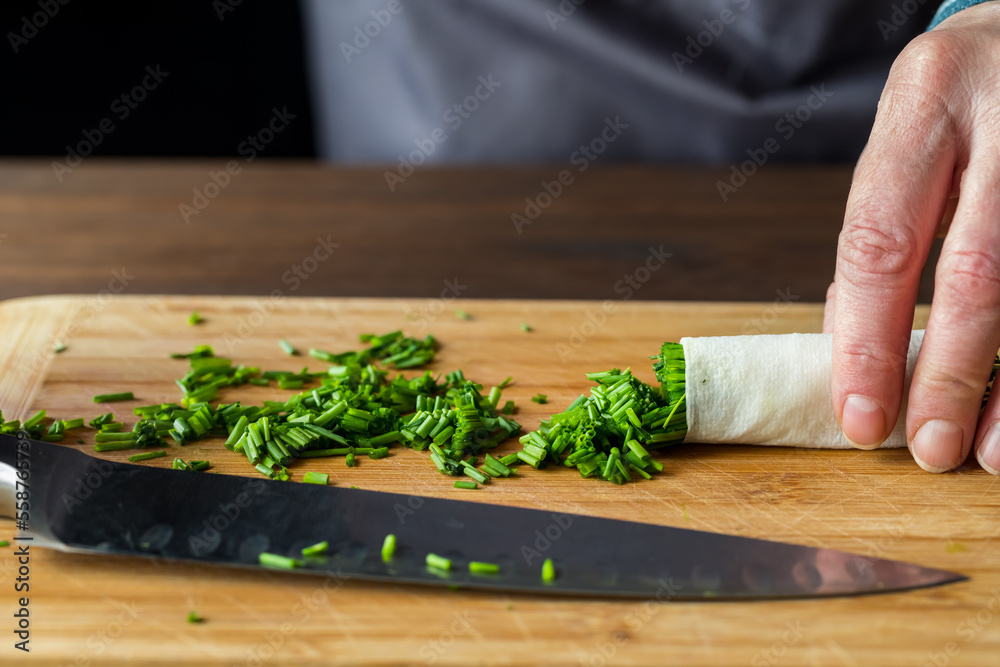 Chopped chives on a wooden cutting board with a sharp knife in front