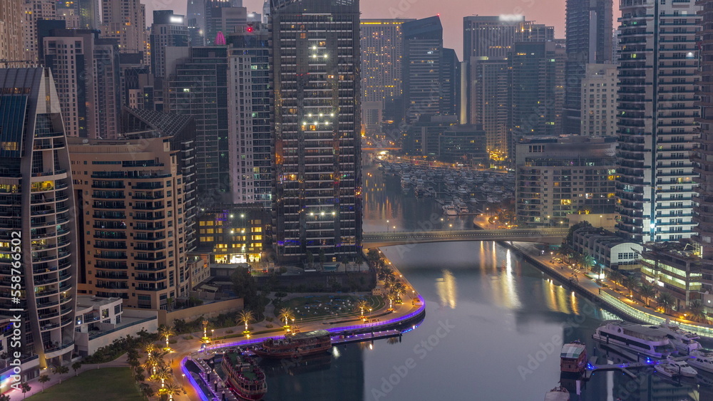 Obraz premium Dubai Marina with several boats and yachts parked in harbor and skyscrapers around canal aerial night to day timelapse.