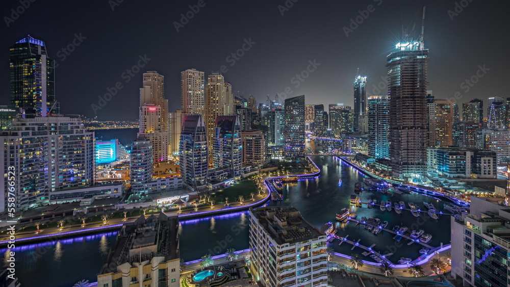 Panorama showing Dubai Marina with several boat and yachts parked in harbor and skyscrapers around canal aerial night timelapse.