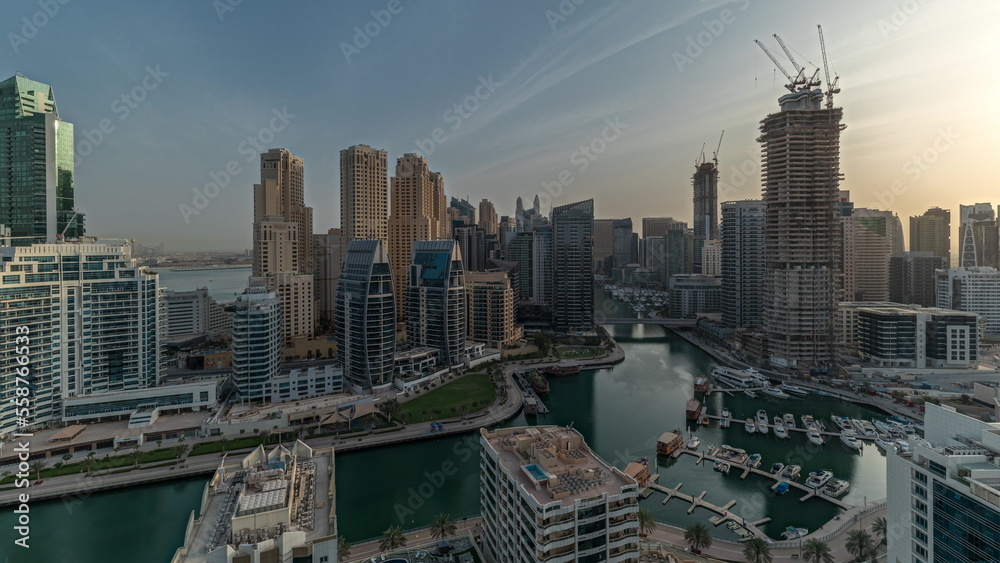 Fototapeta premium Panorama showing Dubai Marina with several boats and yachts parked in harbor and skyscrapers around canal aerial morning timelapse.