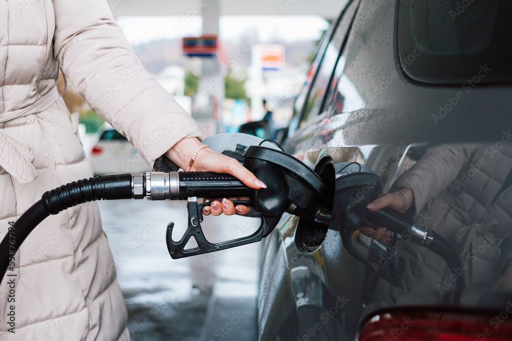 Woman pumping gasoline fuel in car at gas station. Petrol or gasoline price increase concept.