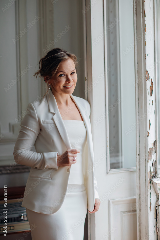 a beautiful, confident woman in a white suit at the old window. image of bride a beautiful, confident woman in a white suit at the old window. image of bride