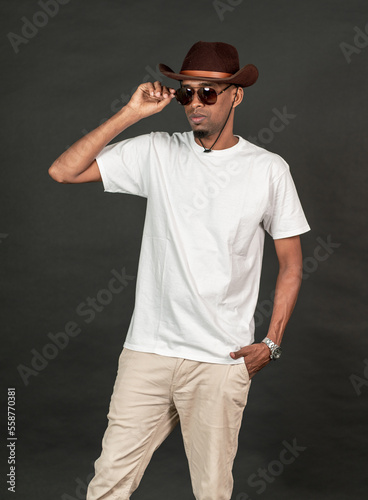 A young man wearing white blank shirt with a glasses and a hat, doing a pose with on of his hand on his glasses