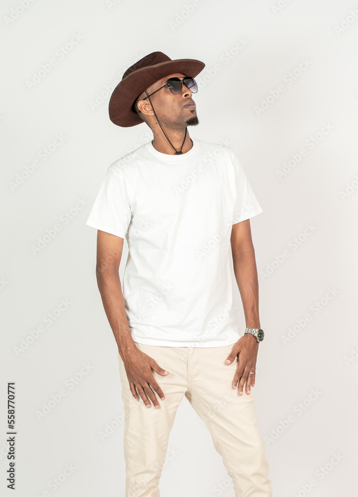 A young african man wearing white blank shirt, with glasses and a hat doing a pose with both of his hand on the front
