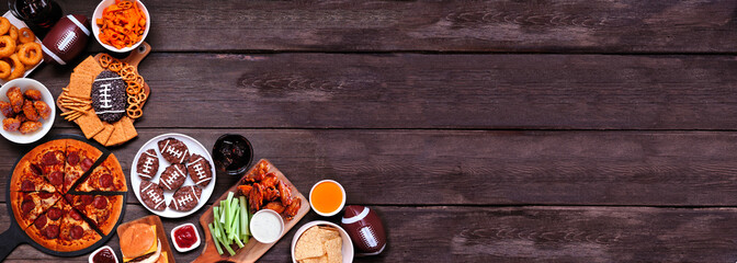 Superbowl or football theme food corner border. Pizza, hamburgers, wings, snacks and sides. Top view on a dark wood banner background.