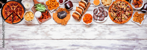 Super Bowl or football theme food top border. Pizza, hamburgers, wings, snacks and sides. Above view on a white wood banner background.