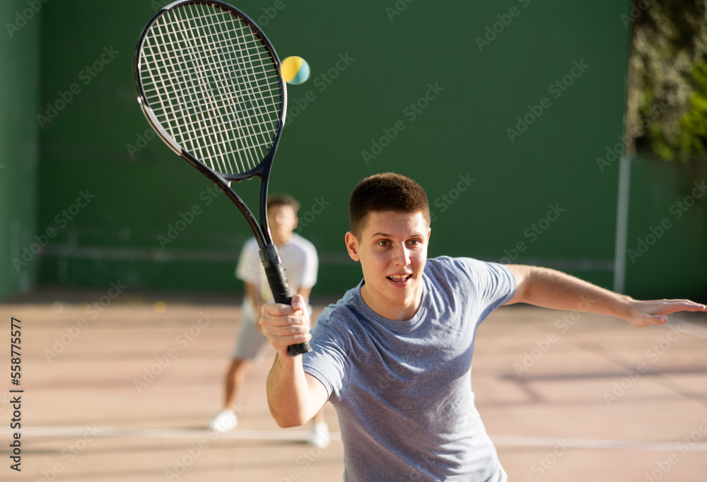Sporty young man playing popular team game frontenis at open-air fronton  court on summer day, ready to hit rubber ball with racquet Stock Photo |  Adobe Stock