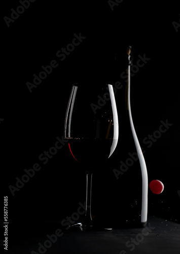 Elegant red wine glass and a wine bottle with red cherry isolated on the black background. bottle silhouette