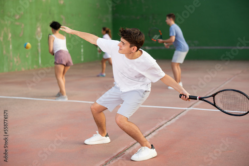 Concentrated young Latin American frontenis player swinging string racquet to hit ball on outdoor walled court on sunny summer day. Sport and active lifestyle concept © JackF