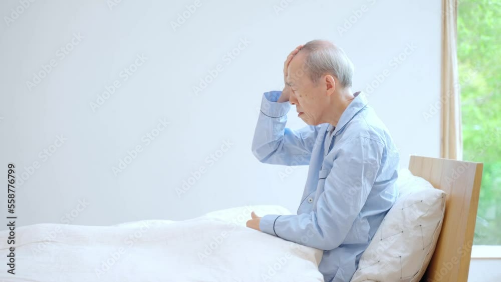 ベッドで頭を押さえる高齢者 ベッドで頭を押さえる高齢者
