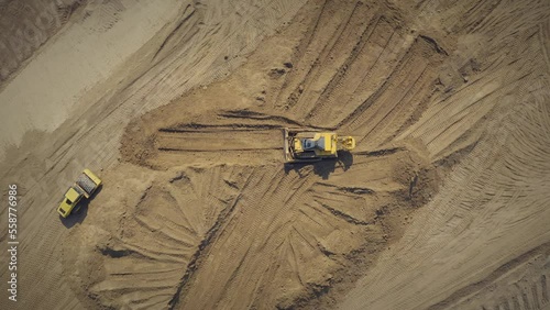 Road construction equipment works on the construction site: a road roller and a bulldozer prepare the sand base for the construction of the road. Top view drone overhead shot.